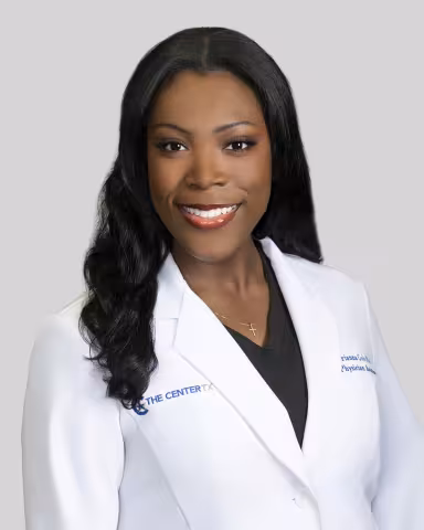 Person in a white lab coat with long, wavy dark hair on a gray background.