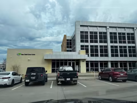 Cars parked in front of a modern office building under a cloudy sky.
