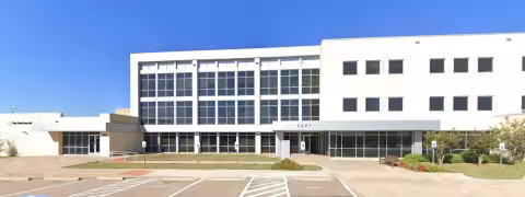 Modern building with large windows and empty parking spaces under a clear blue sky.