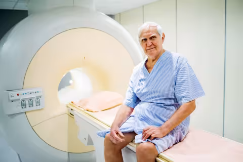 Elderly patient in a hospital gown sitting on an MRI scanner bed.
