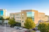 Modern medical building with glass windows, surrounded by trees and parked cars.