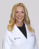Blonde woman in white medical coat with blurred face on gray background.