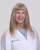 Person in white lab coat with long blonde hair, blurred face, neutral background.