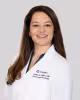 Smiling woman in a white medical coat against a light gray background.