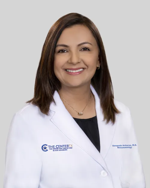 Person in a white medical coat with brown hair, neutral background.
