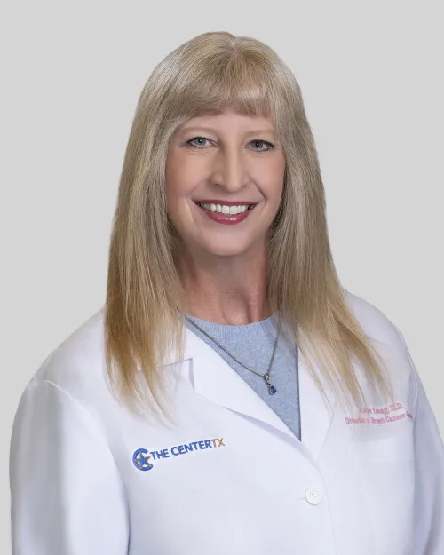 Person in white lab coat with long blonde hair, blurred face, neutral background.