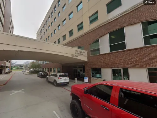 Red truck and white SUV parked outside a hospital building with a skybridge overhead.